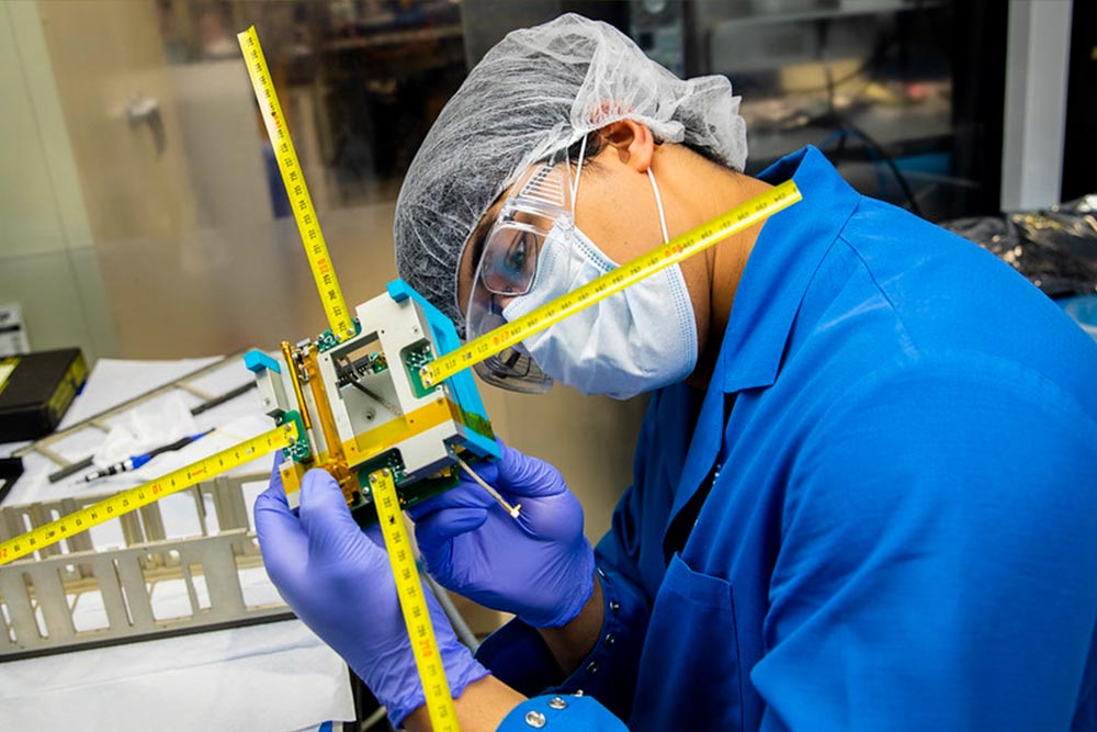person at a laboratory bench working on a satellite prototype