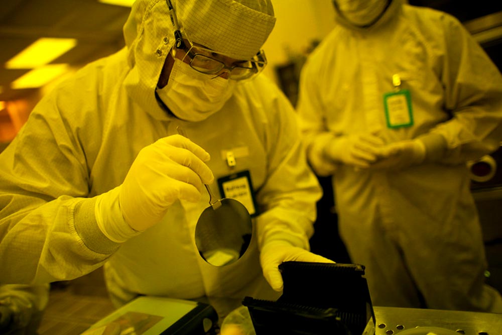 person in full protective suit and glasses moving a reflective disc with a pair of tongs